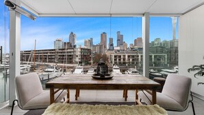 A modern dining area with a city view, a wooden table, two chairs, and a decorative vase. - Waterfront Marina Retreat – Pool, Gym & Parking (Auckland City)