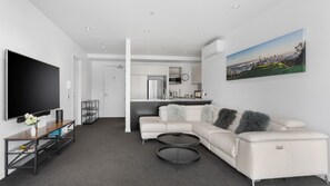 Uma sala de estar moderna com televisão de tela plana, sofá, mesa de centro e área de cozinha ao fundo.