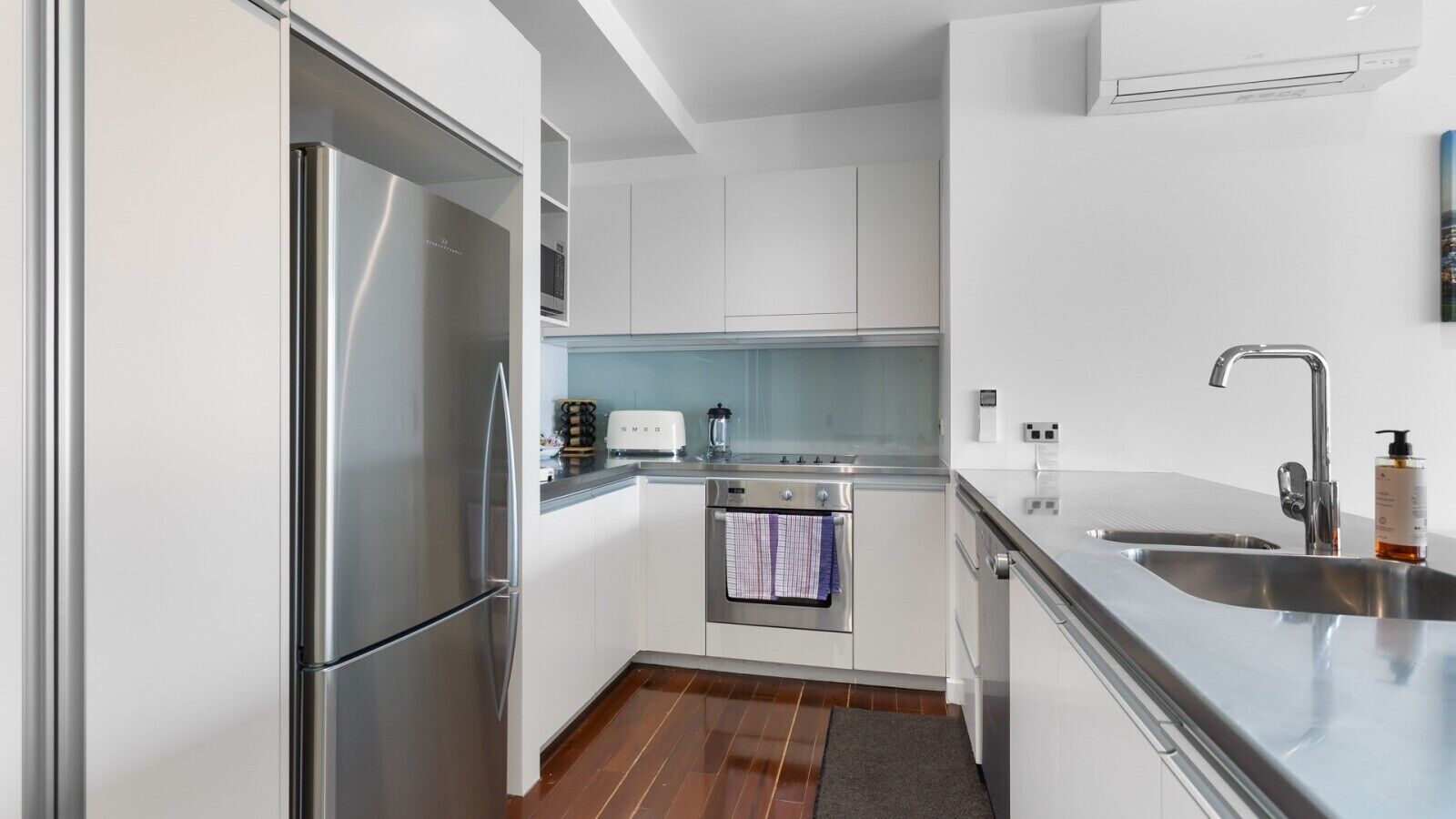 A compact kitchen with a stainless steel refrigerator, a built-in oven, a microwave, and a sink with a faucet.