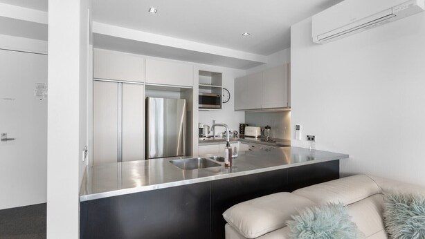 A modern kitchen with a stainless steel island, built-in appliances, and a minimalist design. - Waterfront Marina Retreat – Pool, Gym & Parking (Auckland City)