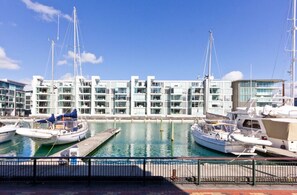 Ein Yachthafen mit mehreren angedockten Booten, ein modernes Gebäude mit Balkonen und einem strahlend blauen Himmel.