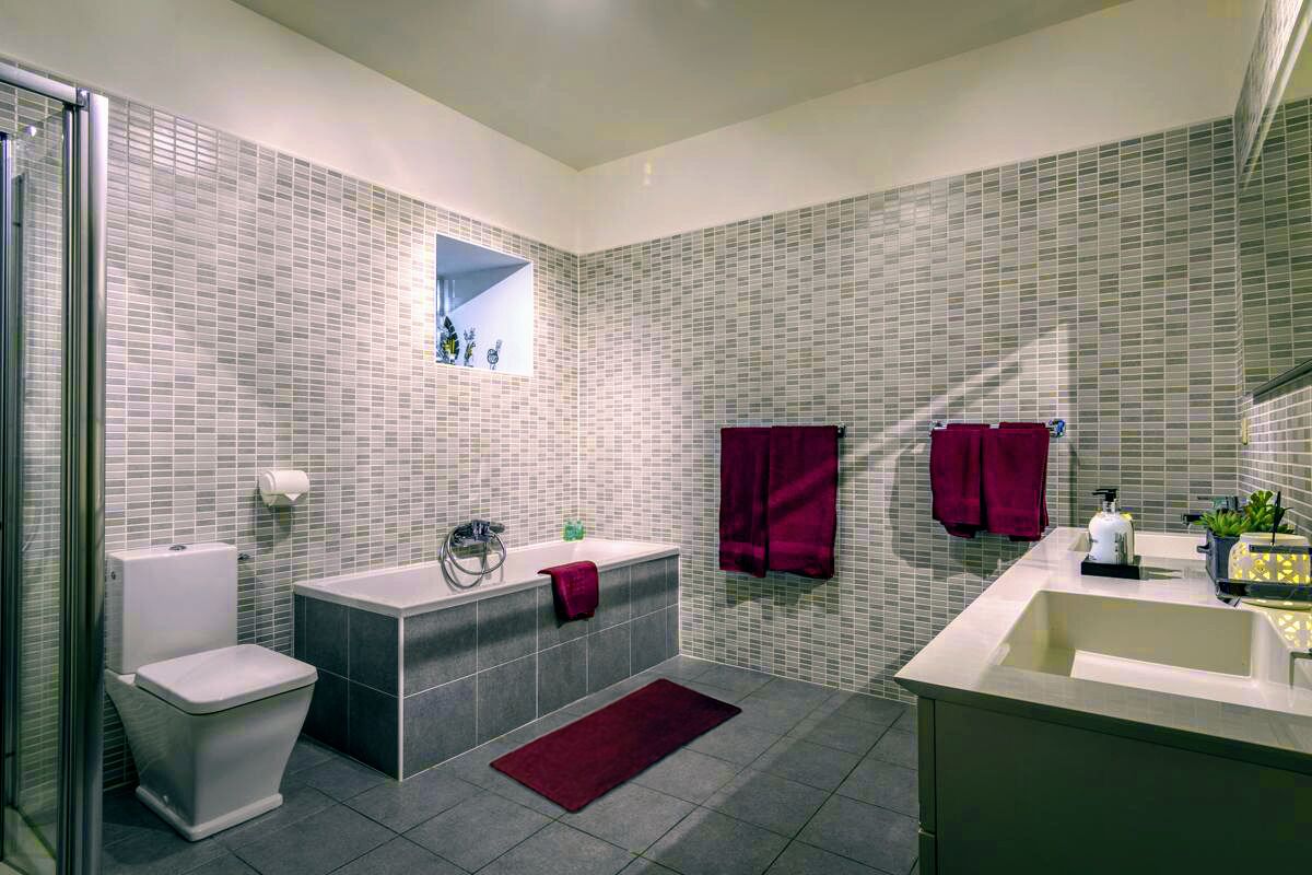 Une salle de bain moderne équipée de toilettes, d’une baignoire et d’un lavabo, avec des murs carrelés et une petite fenêtre.