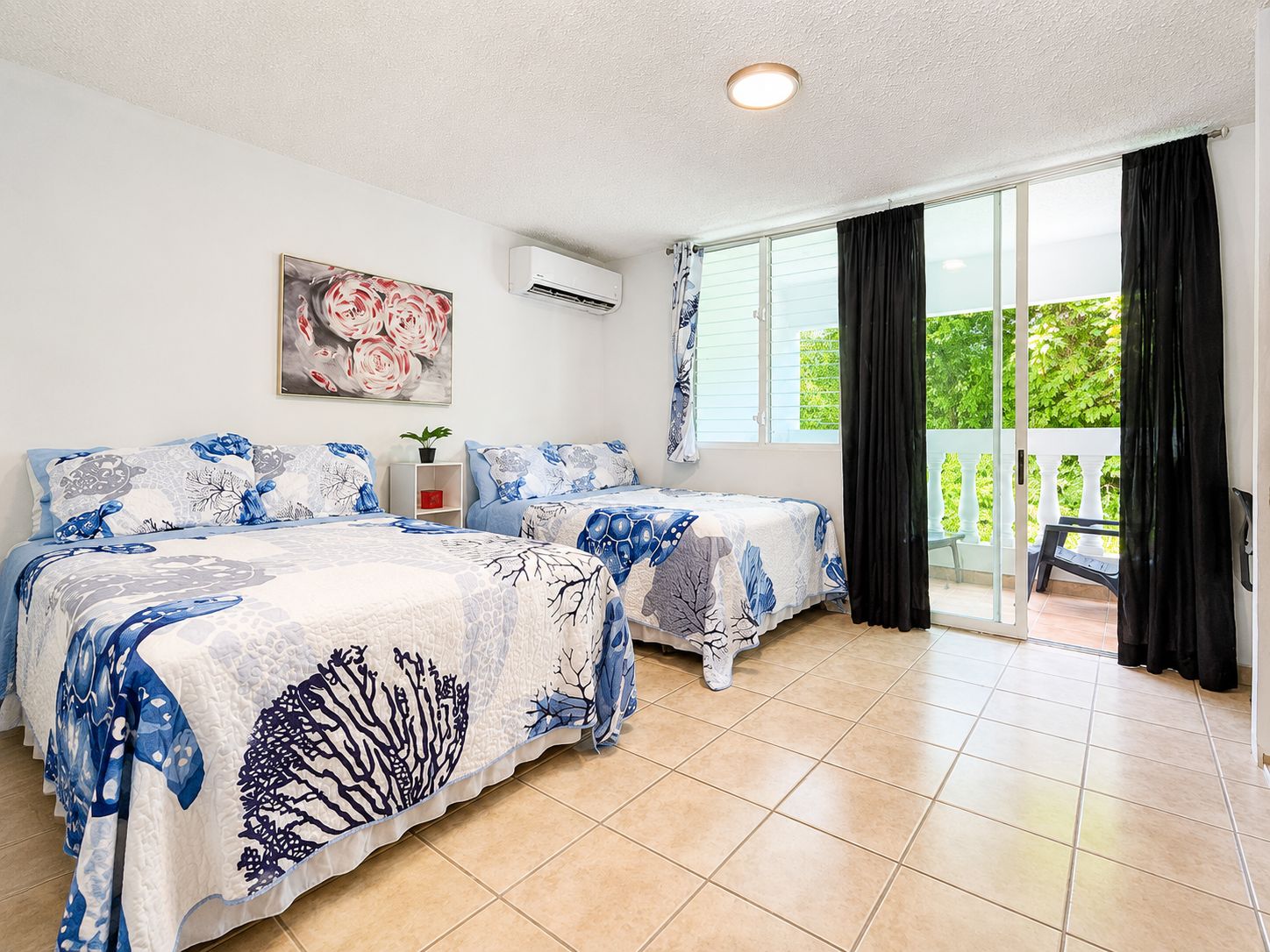 Un dormitorio con dos camas, ventilador de techo, ventana con cortinas y balcón con una silla.