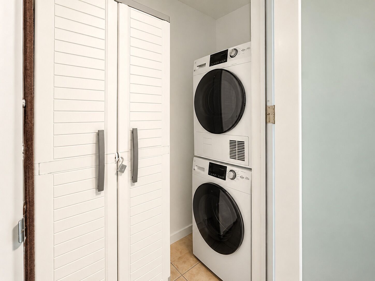 A laundry room with two stacked front-loading washing machines and a white door with a handle.