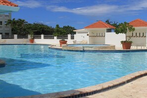 A swimming pool with a tiled edge, surrounded by white buildings with red-tiled roofs and potted plants.