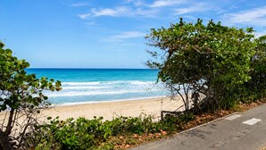A beach with clear blue water, a sandy shore, and a road with a sidewalk. - Golden Dream Studio 2nd floor B (Isabela)