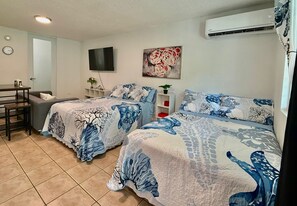 A bedroom with two beds, a desk, a chair, a TV, and an air conditioner.
