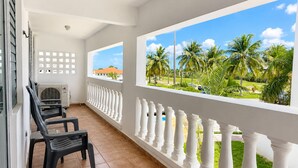 A balcony with white balustrades, a view of palm trees, and a building with an orange roof. - Golden Dream Studio 2nd floor B (Isabela)