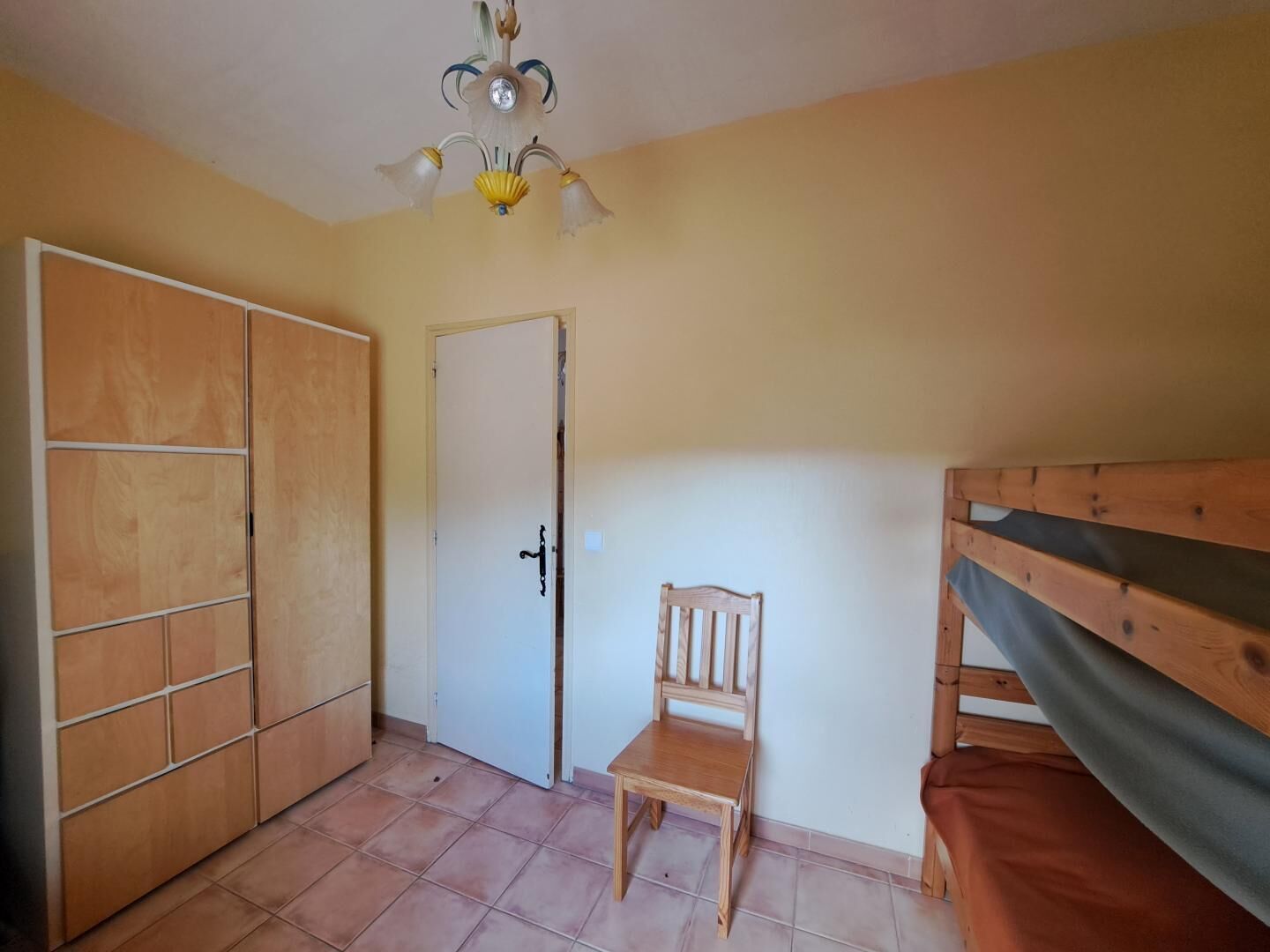Een kamer met een houten kledingkast, een deur, een kleine houten stoel en een stapelbed.