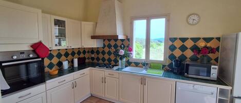 Une cuisine avec des meubles blancs, une cuisinière, un four à micro-ondes et une fenêtre donnant sur un beau paysage.