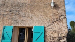 Un edificio con fachada texturizada, dos ventanas con persianas turquesas y un pequeño aplique de pared.