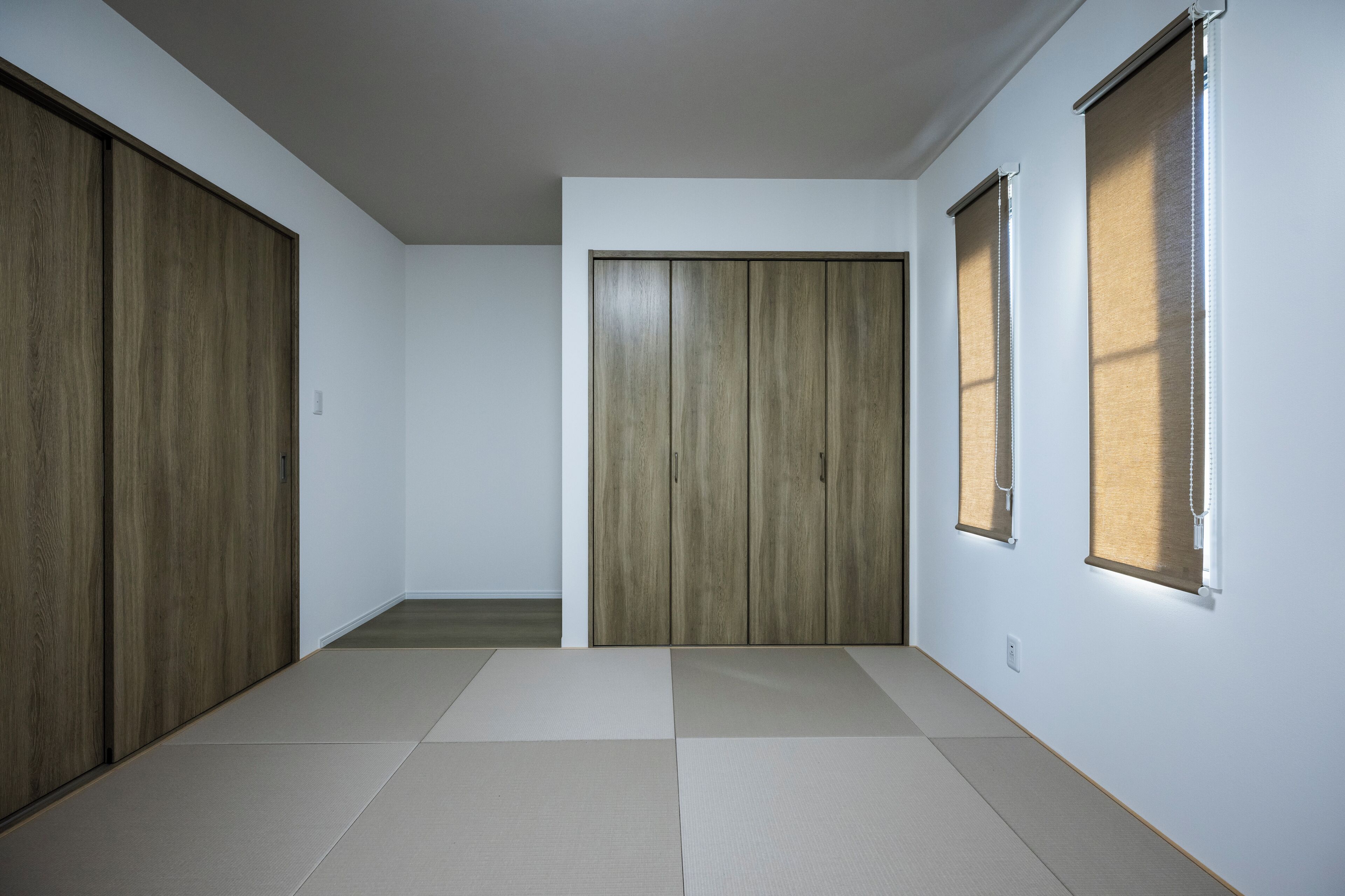 Ein Zimmer mit einer Holztür, die sich verschieben lässt, einem Fenster mit Jalousien und einem Teppichboden aus Tatami-Matten.