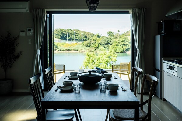 Comedor con una mesa lista para cuatro, vista a un lago y zona de cocina.