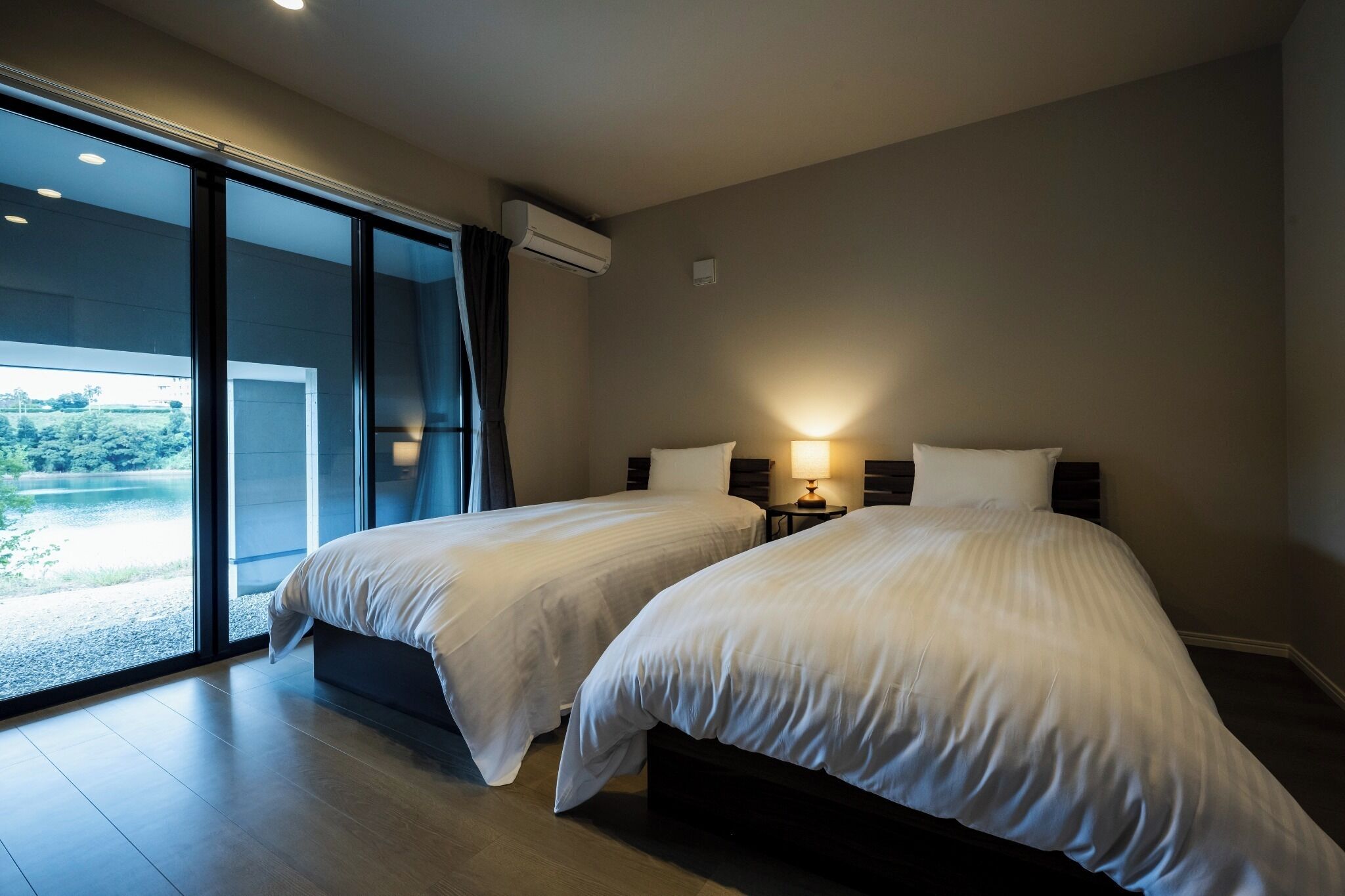 A hotel room with two beds, a large sliding glass door leading to a balcony, and a wall-mounted air conditioner.