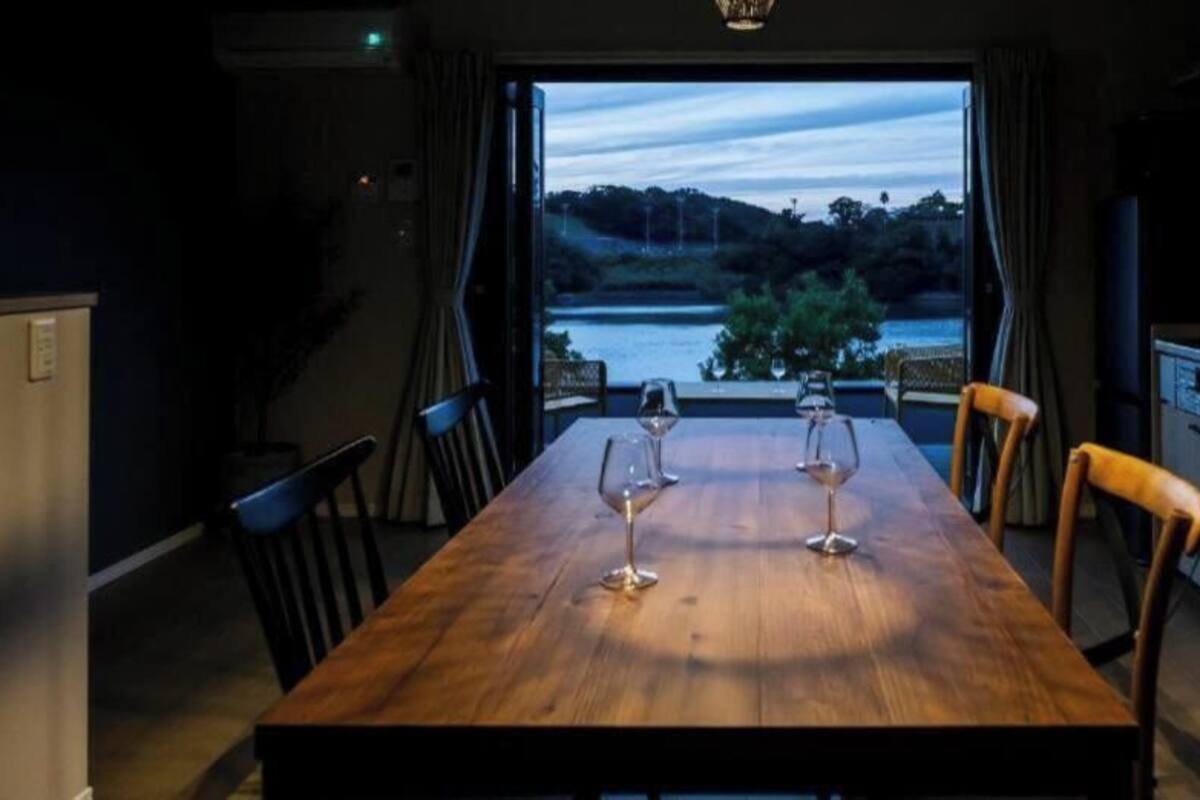 A dining table with two wine glasses, a view of a lake, and a kitchen area with cabinets and a TV.