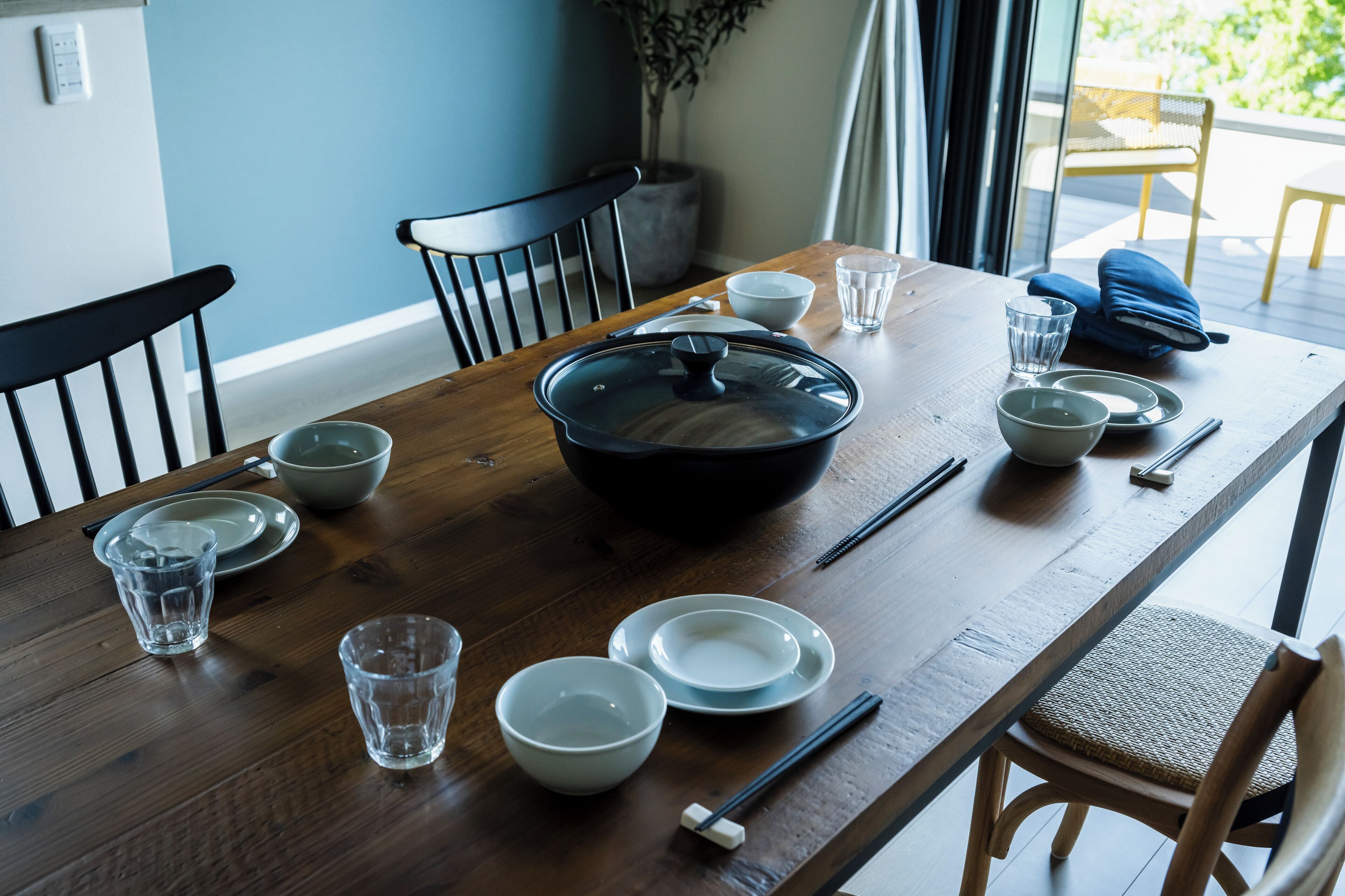 Et spisebord dækket med skåle, spisepinde og glas, med stole derom.