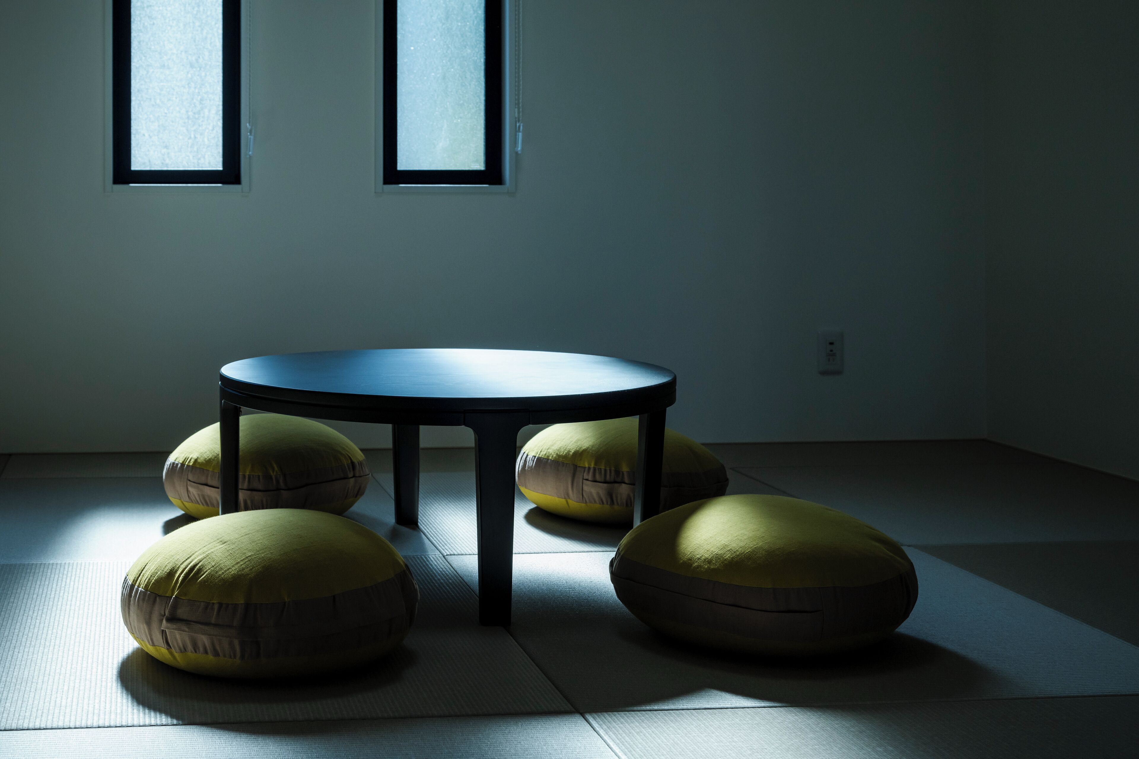 A room with tatami flooring, a round table, and four cushions.