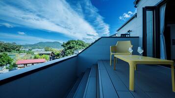 A balcony with a view of a lake and mountains, a yellow table, and two chairs.