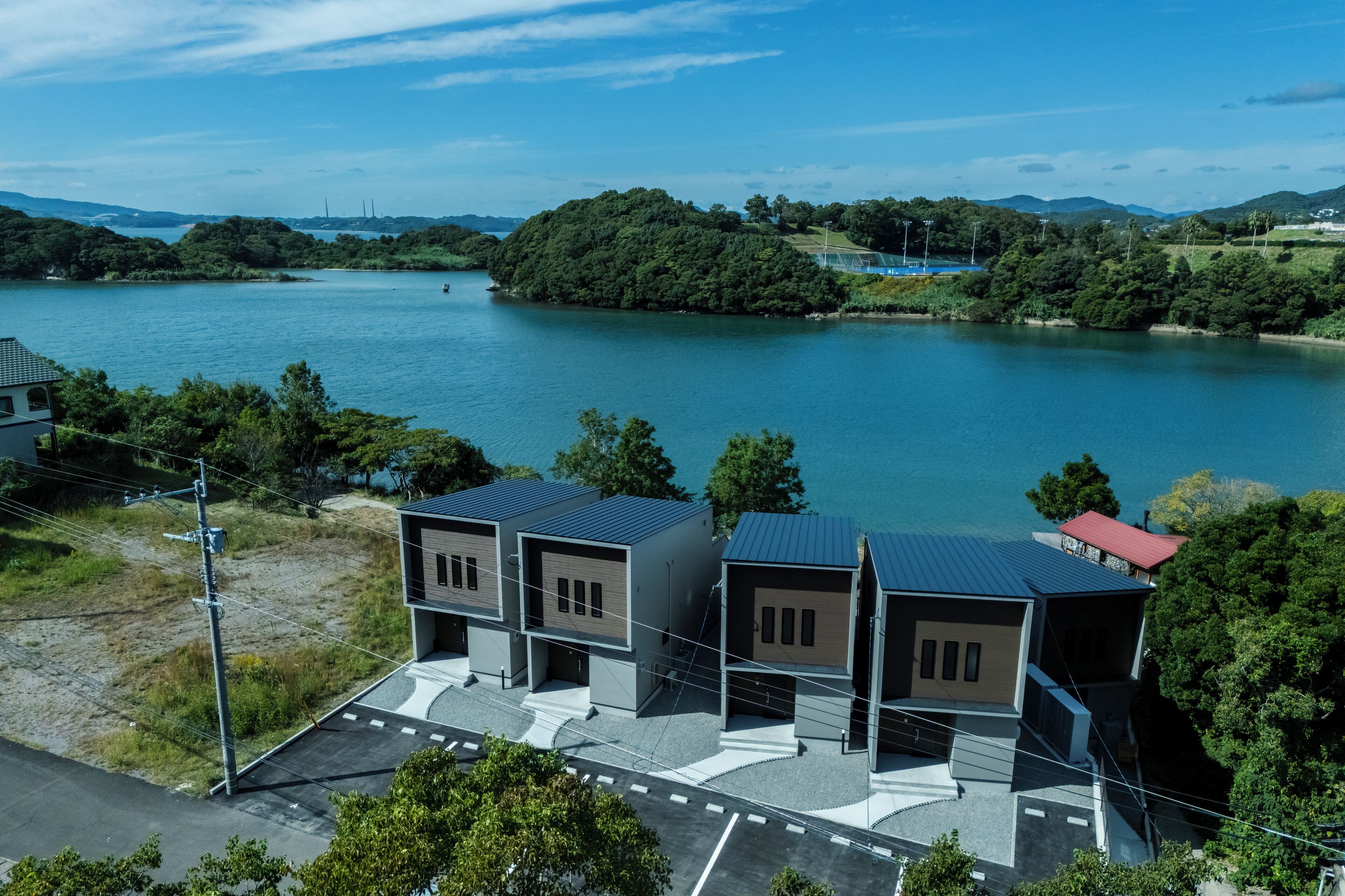 A modern building with a flat roof and a red roofed section, situated near a body of water with a forested island in the background.
