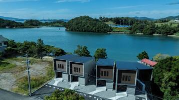 A modern building with a flat roof and a red roofed section, situated near a body of water with a forested island in the background.
