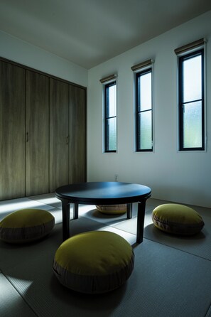 Una habitación con una mesa redonda, tres ventanas y un armario de madera.
