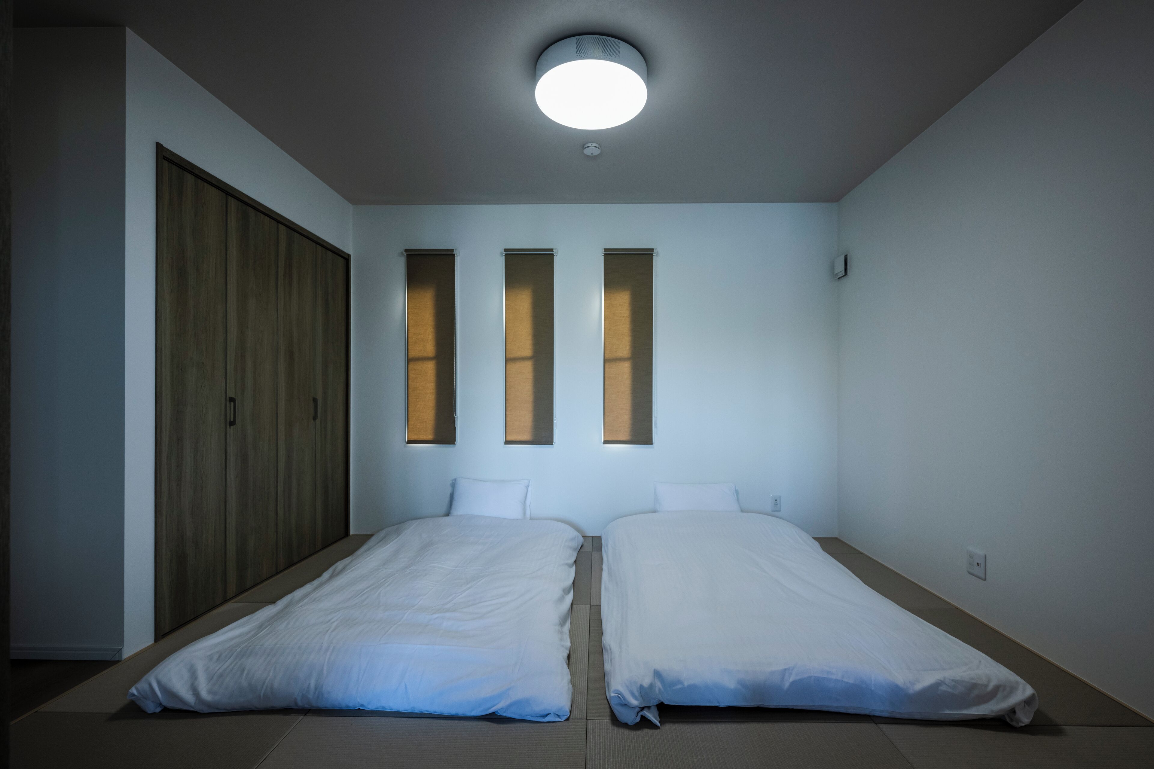 A room with two beds, a wardrobe, and three windows.