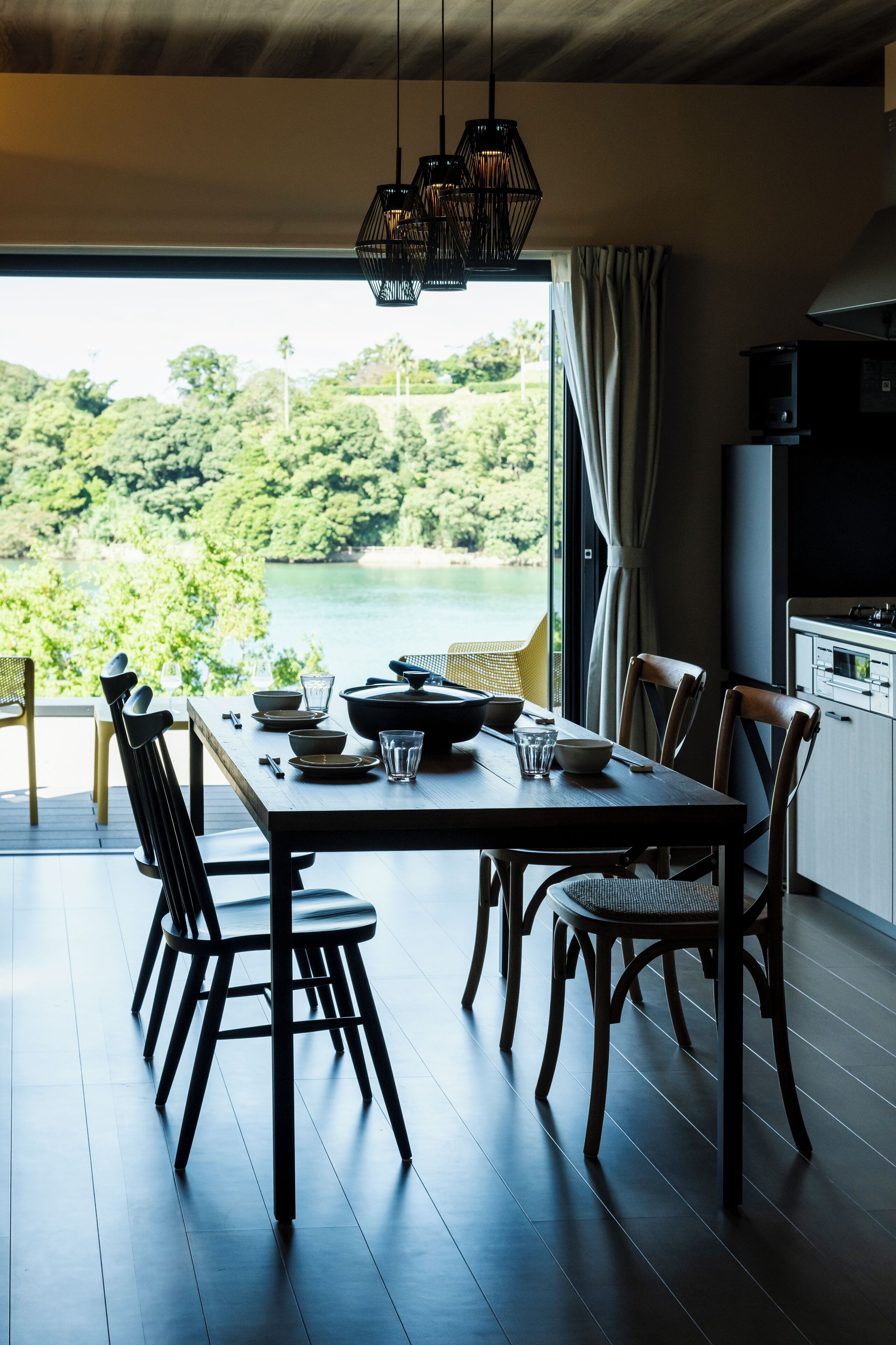 A dining area with a table set for four, surrounded by chairs, a view of a lake, and a kitchen area with a stove and cabinets.