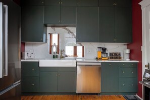 Una cocina con armarios verde oscuro, encimera blanca y lavavajillas de acero inoxidable.