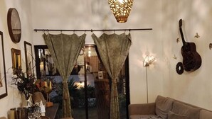 A cozy living room with a sofa, a dining table with chairs, a guitar wall decoration, and a large window with curtains. - LAS AVES (Juayua)