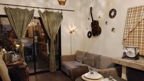 A cozy living room with a brown sofa, a round table with decorative plates, and a guitar on the wall. - LAS AVES (Juayua)
