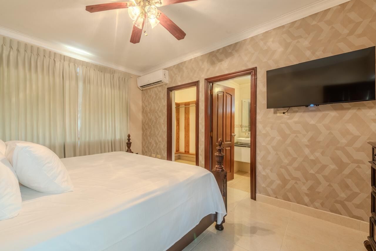 Hotelkamer met een bed, een plafondventilator, een flatscreen-televisie aan de muur en een deur naar een badkamer.