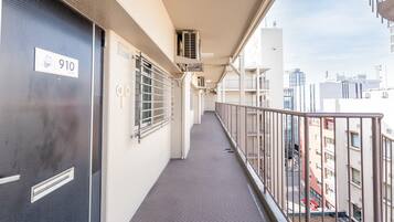 A corridor with a metal railing, a door labeled '910', and a view of the cityscape in the background.