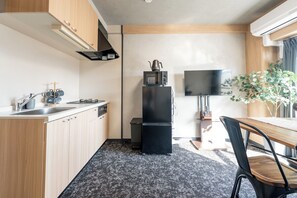 A compact kitchen with a microwave, stove, and sink. There is a small table and a chair. - b&Shin-Osaka (Osaka)