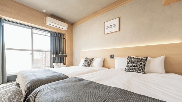 A hotel room with two beds, a large window with curtains, an air conditioning unit, and a framed picture on the wall. - b&Shin-Osaka (Osaka)