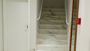 A marble-floored hallway leading to a staircase with a white door and a mirror on the wall. - Fully furnished apartment (Rio do Sul)