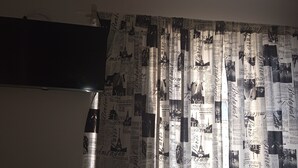 A room with a flat-screen TV mounted on the wall and a curtain with cityscape prints. - Fully furnished apartment (Rio do Sul)
