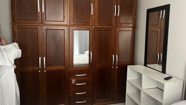 A bedroom with a large wooden wardrobe, a mirror, and a white bedside table. - Fully furnished apartment (Rio do Sul)
