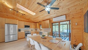 A modern kitchen with wooden cabinets, stainless steel appliances, and a dining area with white chairs. - New to VRBO! Lakefront I Movie Theater I Putting Green I Game Room I Bocce ball! (White Haven)
