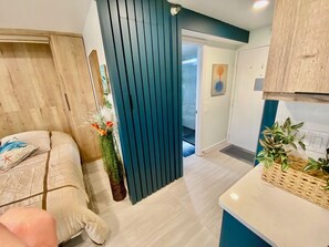 A modern bedroom with a bed, a wooden headboard, a blue partition, and a small balcony with a view. - Stunning Brand New Studio - Balcony w/ Scenic Ocean and Sunset Views-Heated pool (Daytona Beach)