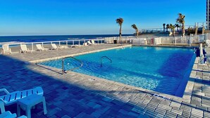 Un espace piscine avec vue sur l’océan, des chaises longues blanches et des palmiers.