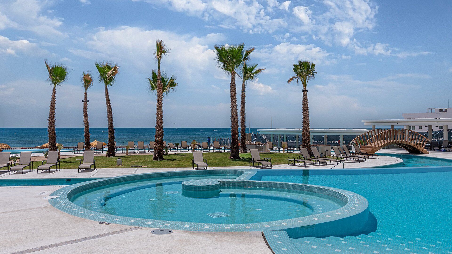 A pool area with palm trees, lounge chairs, and a view of the ocean.