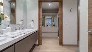 Un baño moderno con encimera de mármol, un espejo grande y una puerta de madera que da a un pasillo.