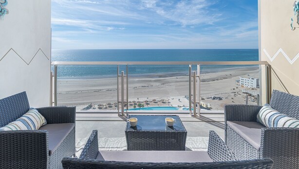 A balcony with wicker furniture, a glass table, and a view of the beach and ocean. - One 1502 Full– Beach Paradise with First-Class Comfort and Ocean Views (Puerto Peñasco)