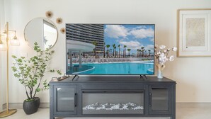 A television displaying a resort pool area with palm trees and a modern building. - One 1502 Full– Beach Paradise with First-Class Comfort and Ocean Views (Puerto Peñasco)