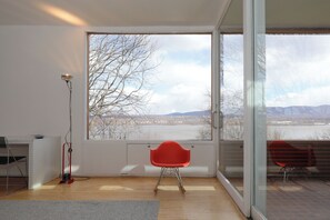 Ein Zimmer mit einem großen Fenster, einem roten Sessel, einer Stehlampe und einem kleinen Tisch.