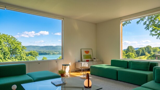 Uma sala de estar moderna com sofás verdes, uma mesa de centro de vidro e vista para um lago e montanhas.