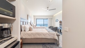 A modern hotel room with a large bed, a ceiling fan, a kitchenette, and a view of the ocean. - One 1502 Hotel Room – New Seaside Gem Delivering Style, Comfort, and Panoramic Views (Puerto Peñasco)