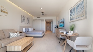 Une chambre d’hôtel moderne, équipée d’un lit, d’un canapé, d’un bureau et d’une chaise. Un tableau orne le mur et un ventilateur de plafond est installé au plafond.