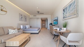 A modern hotel room with a bed, a sofa, a desk, and a chair. There is a painting on the wall and a ceiling fan. - One 903B Studio: Oceanfront Icon of Timeless Luxury at the Newest Resort. (Puerto Peñasco)