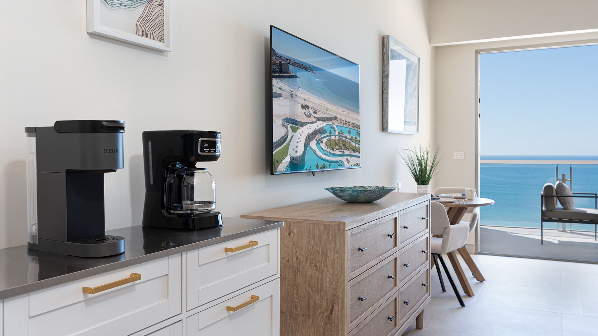 Une cuisine moderne équipée d’une machine à café Keurig, d’un grand tableau représentant un paysage marin encadré, et offrant une vue sur l’océan.